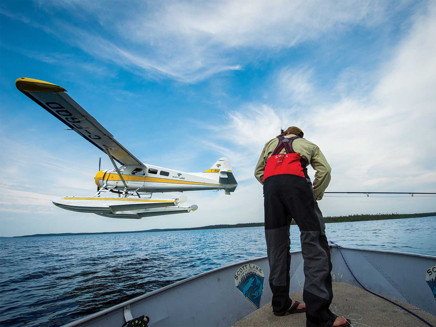 Angler fishing off of a boat while biplane flies overhead.